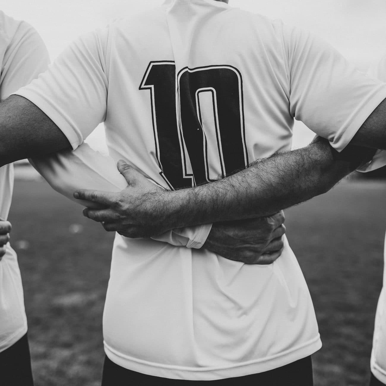 Teammates in white shirts standing arm in arm before kickoff